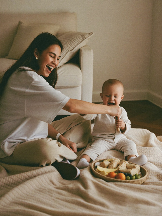 A mom laughing with her baby over a small indoor picnic